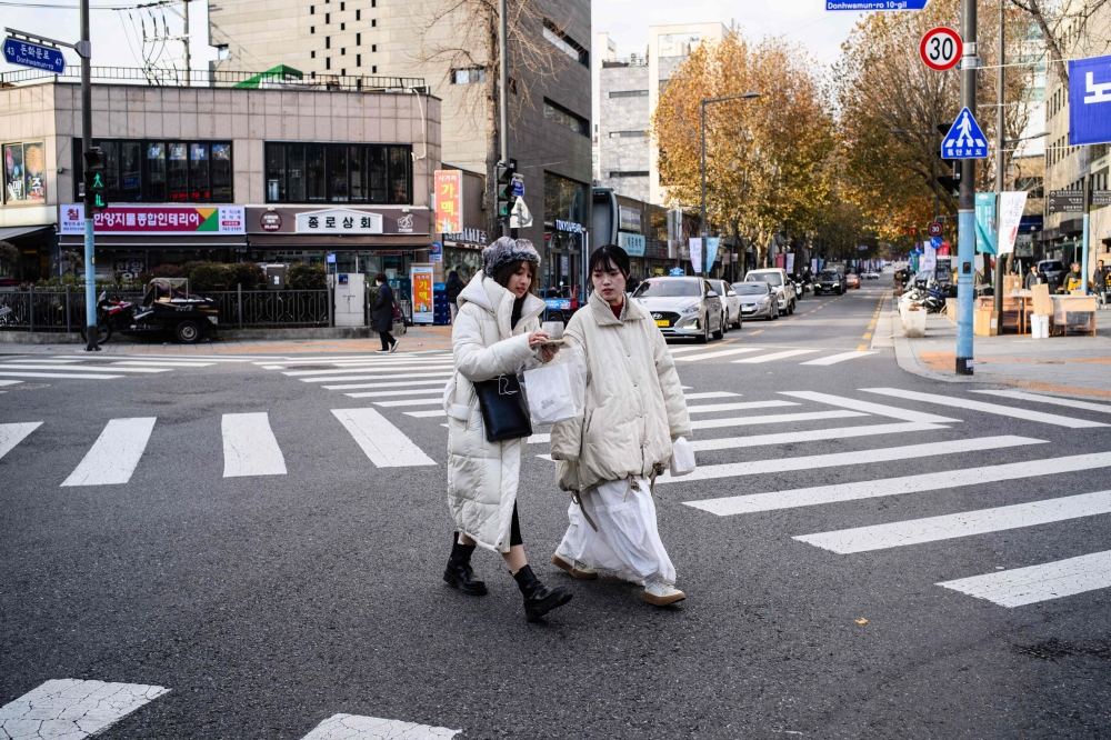 File of two women walking across a road in the Jongno district of Seoul on December 4, 2023. — AFP pic