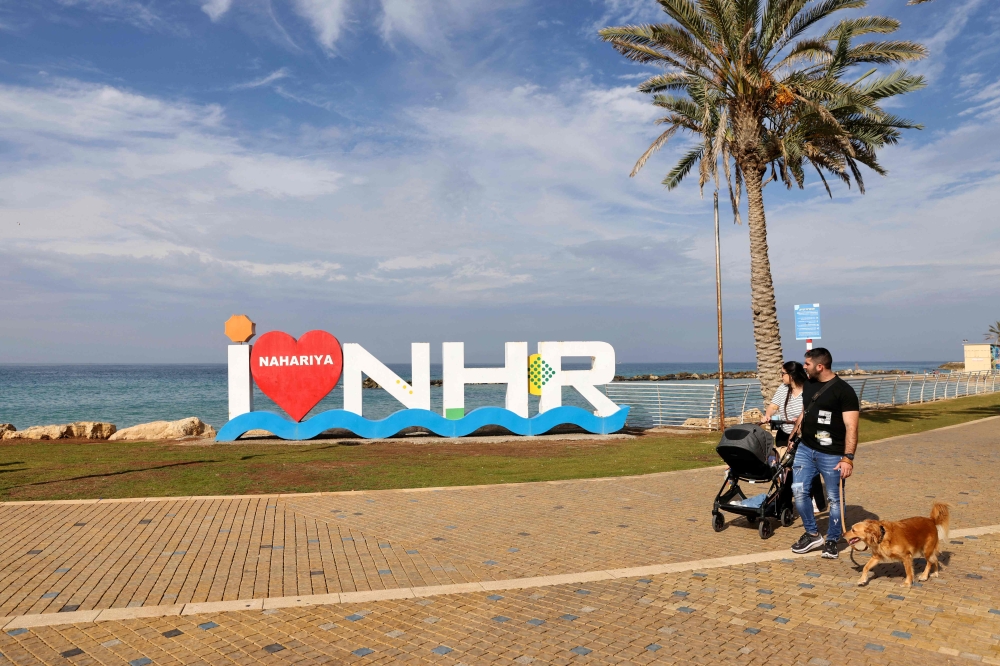 An armed Israeli man walks with his family in the northern coastal Israeli city of Nahariya near the border with Lebanon on December 8, 2023, amid ongoing cross-border tensions as fighting continues with Hamas militants in the southern Gaza Strip. — AFP pic