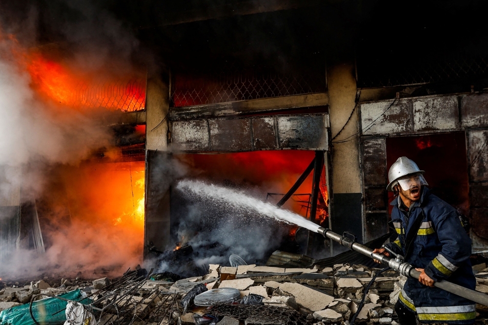A Palestinian firefighter works to extinguish a fire in a house after an Israeli strike. — Reuters pic