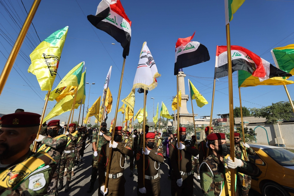 Fighters lift flags of Iraq and paramilitary groups, including al-Nujaba and Kataib Hezbollah, during a funeral in Baghdad for five militants killed in a US strike in northern Iraq on December 3, 2023. — AFP pic