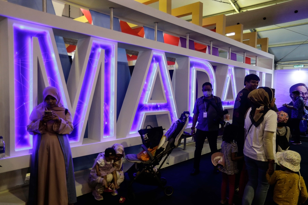People walk by the Madani logo during the Madani Government One Year Anniversary programme at Bukit Jalil National Stadium December 10, 2023. — Picture by Sayuti Zainudin