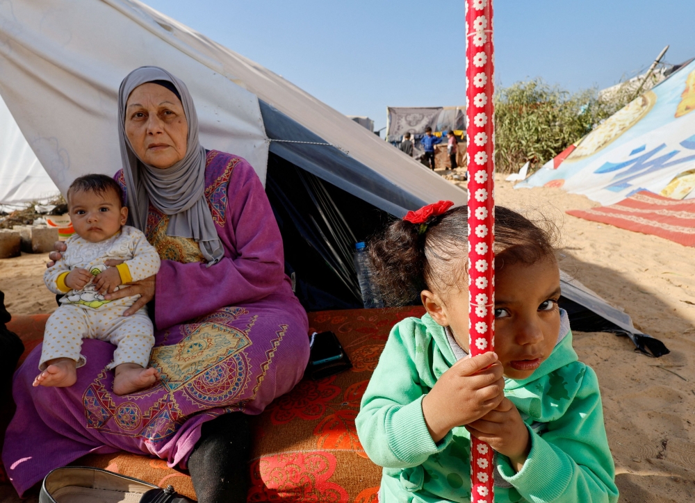 A woman holds a baby next to a girl, as displaced Palestinians, who fled their houses due to Israeli strikes, shelter in a tent camp near the border with Egypt, amid the ongoing conflict between Israel and the Palestinian Islamist group Hamas, in Rafah in the southern Gaza Strip, December 11, 2023. — Reuters pic