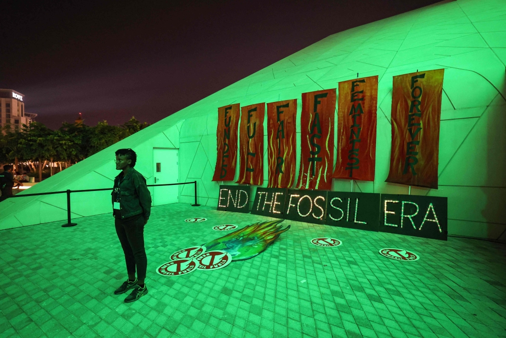 A woman poses in front of banners against fossil fuels outside Expo City in Dubai on December 12, 2023 during the United Nations Climate Change Conference COP28. — AFP pic