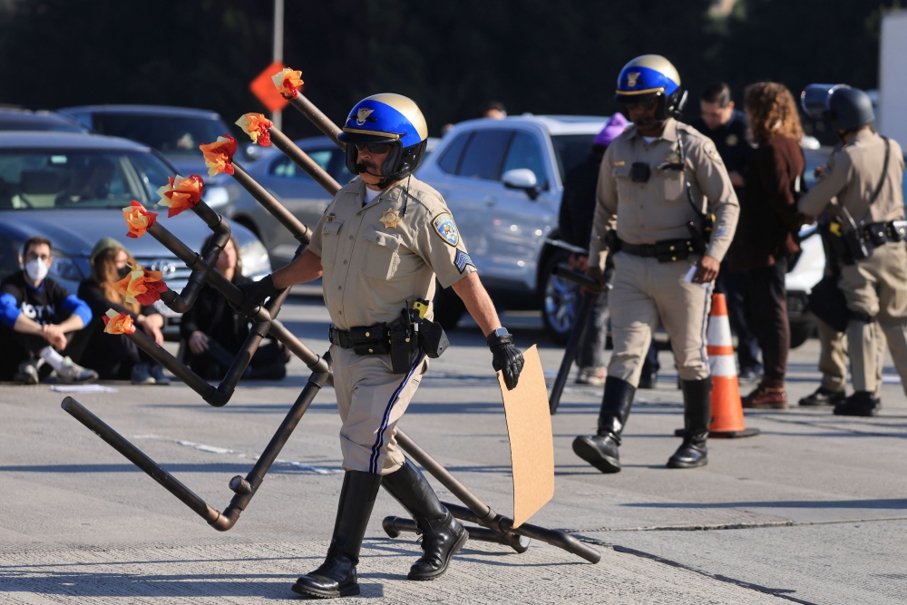 A law enforcement officer removes a Hanukkiyah, a candlestick with nine branches that is lit to mark Hanukkah, placed by demonstrators demanding a ceasefire and an end to US support for Israel's attack on Gaza to block morning traffic on the 110 Freeway, in Los Angeles December 13, 2023. — Reuters pic