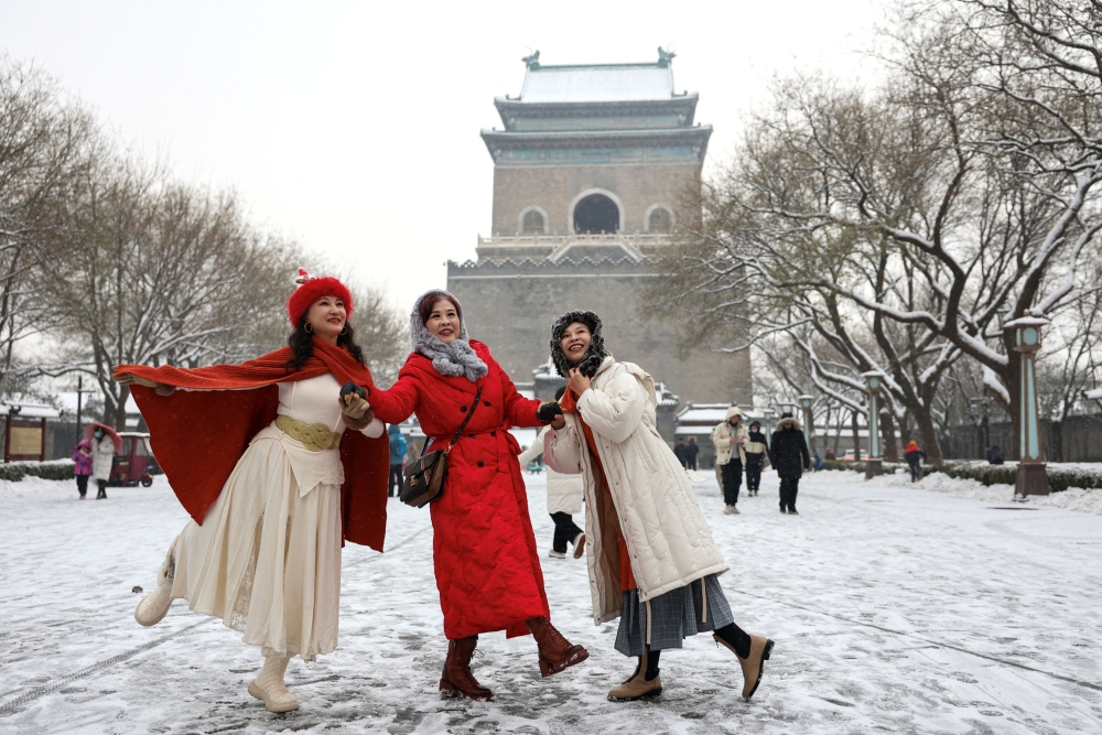 Women pose for pictures near the Bell Tower amid snowfall in Beijing December 13, 2023. — Reuters pic