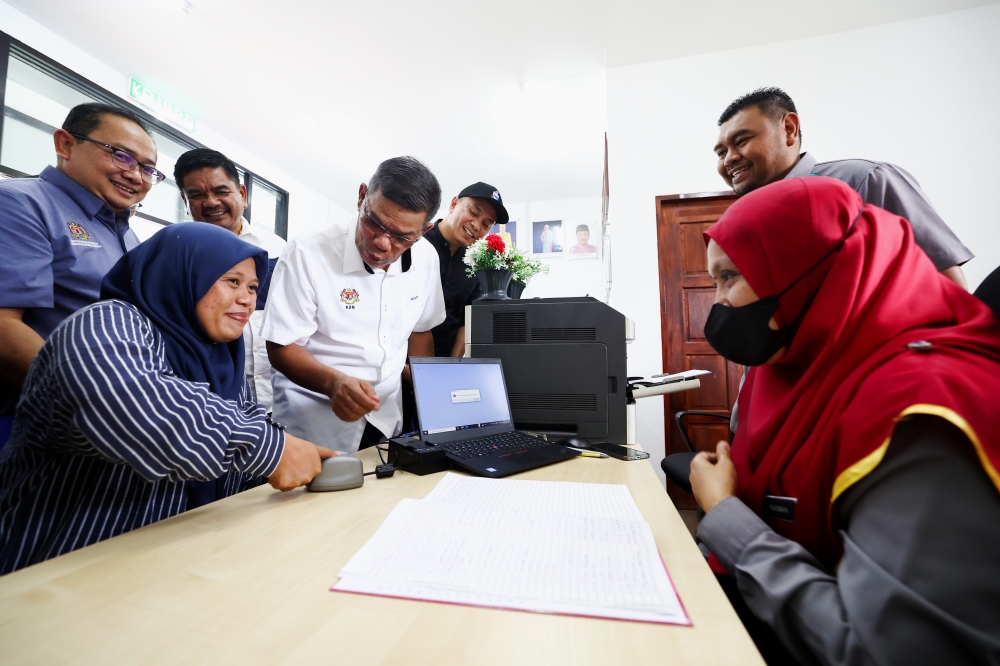 Home Minister Datuk Seri Datuk Seri Saifuddin Nasution Ismail (centre) observes as Jumatiah Osman scans her fingerprint while applying for an identity card replacement after opening the Kalabakan branch National Registration Department office and department’s outreach programme December 15, 2023. — Bernama pic 