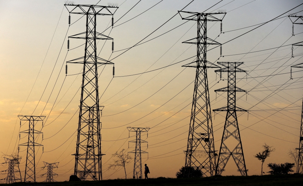 A man walks beneath electricity pylons during frequent power outages from South African utility Eskom, caused by its ageing coal-fired plants, in Orlando, Soweto, South Africa, January 16, 2023. — Reuters pic  