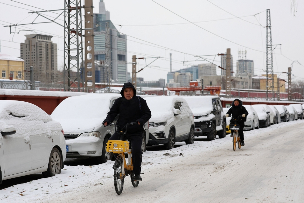 People ride bicycles on a road covered by snow following snowfall in Beijing, China December 15, 2023. — Reuters pic