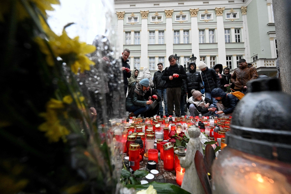 People place flowers and candles at a makeshift memorial for the victims outside the Charles University in central Prague December 22, 2023, as police investigators kept working on the campus the day after a deadly mass shooting. — AFP pic