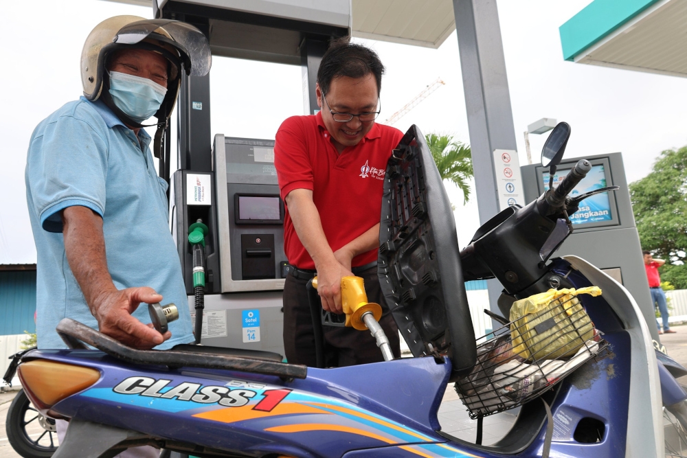Sarawak DAP chairman Chong Chieng Jen helps a motorcyclist refuel his machine at the Petronas Sungai Maong station. — Borneo Post 