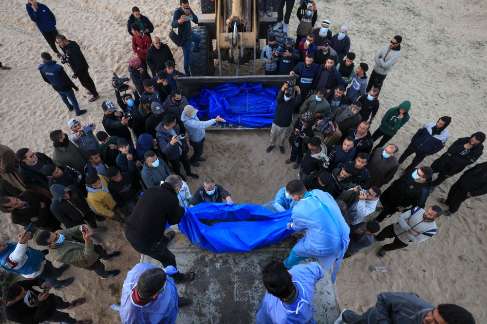 The shrouded bodies of Palestinians killed in nothern Gaza, that were taken and later released by Israel, are unloaded from a container to be burried in a mass grave in Rafah, on the southern Gaza Strip on December 26, 2023, amid ongoing battles between Israel and the militant group Hamas. — AFP pic