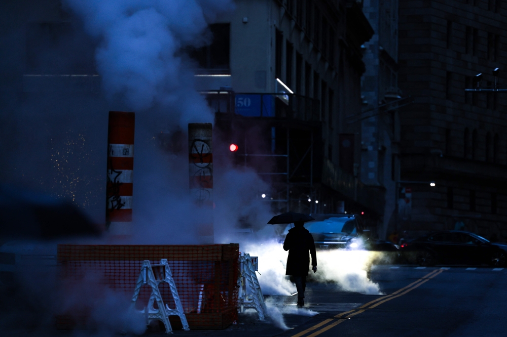A person holds an umbrella as they walk through steam in a street of the Lower Manhattan borough of New York city on December 27, 2023. — AFP pic