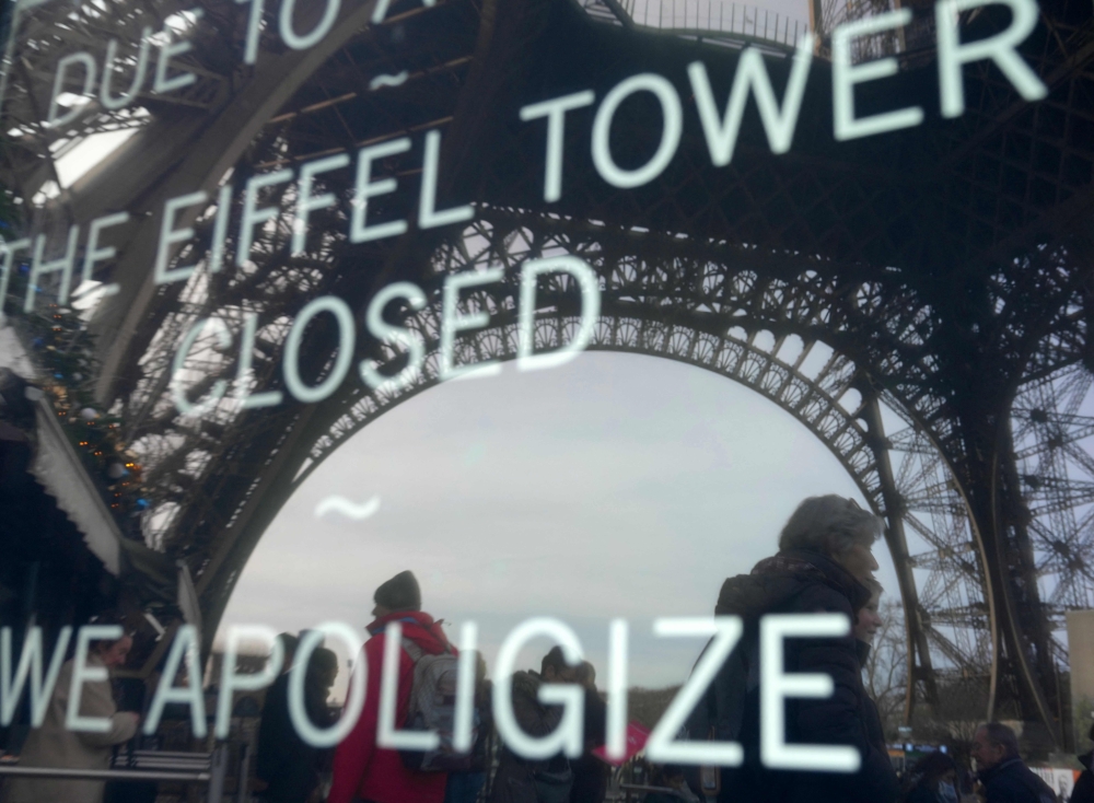 This photograph taken on December 27, 2023 in Paris shows the reflection of tourists and the Eiffel Tower in a board informing visitors that the site is closed after staff went on strike. — AFP pic