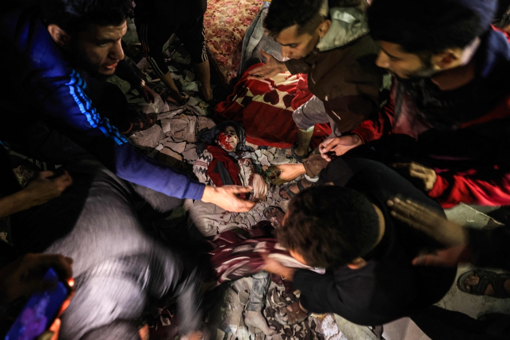 People struggle to remove an injured woman from under the rubble of a building hit by an Israeli strike on Rafah in the southern Gaza strip on December 28, 2023, as battles continue between Israel and the Palestinian Hamas movement. — AFP pic