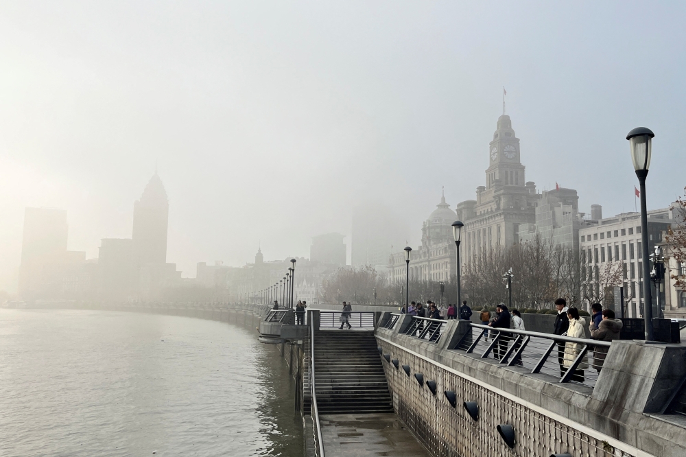 People stand on the Bund as buildings along the Huangpu river are seen shrouded in fog, amid a red alert for heavy fog in Shanghai December 29, 2023. — Reuters pic