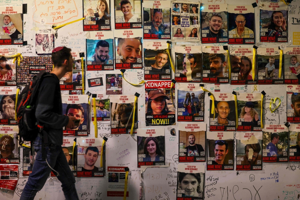 A man walks past a wall showing portraits of Israeli hostages held in Gaza since the October 7 attacks by Hamas in southern Israel, in Tel Aviv December 28, 2023. Some 129 hostages remain in captivity in Gaza. — AFP pic