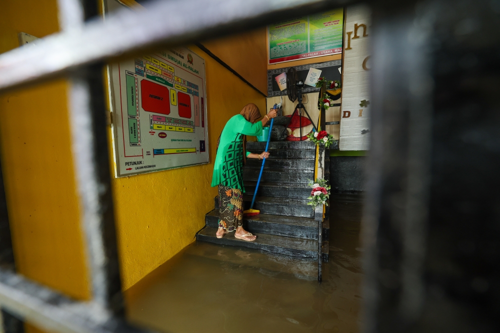 A school cleaner cleans mud marks on the school stairs due to floods that occurred since December 26 at Al-Falah Religious Secondary School (Arab) in Kampung Siram, Pasir Mas, Kelantan, December 30, 2023. — Bernama pic 
