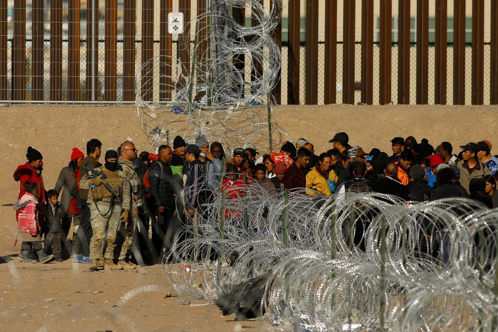 Migrants seeking asylum in the United States gather near the border wall after crossing a razor wire fence deployed to inhibit their crossing into the United States, while members of the Texas National Guard stand guard, as seen from Ciudad Juarez, Mexico January 2, 2024. ― Reuters pic