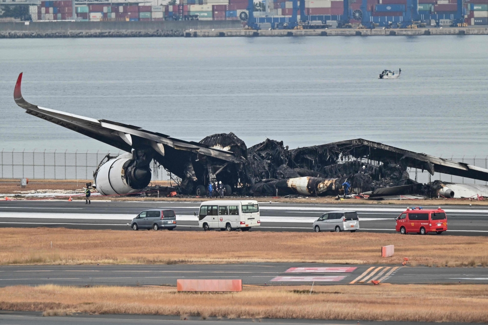 Officials look at the burnt wreckage of a Japan Airlines (JAL) passenger plane on the tarmac at Tokyo International Airport at Haneda in Tokyo on January 3, 2024, the morning after the JAL airliner hit a smaller coast guard plane on the ground. — AFP pic