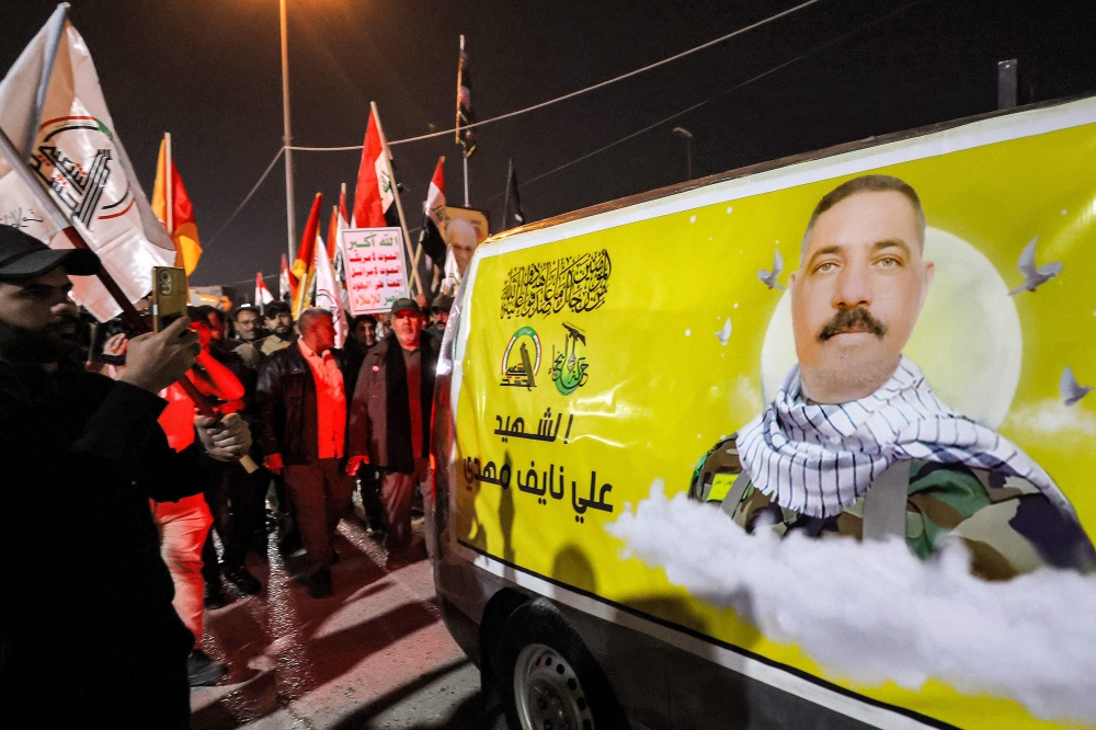 Members of Iraq's Popular Mobilisation Forces (PMF) paramilitaries march alongside a vehicle carrying the body of the group's slain members during the funeral at the PMF headquarters in Baghdad on January 4, 2024. — AFP pic