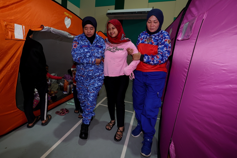 Flood victim and cancer patient Norashikin Nor Azman (centre) is assisted by members of the Civil Defence Force at the Dewan Muafakat Kg Cahaya Baru temporary relief centre in Johor Baru January 5, 2024. — Bernama pic 