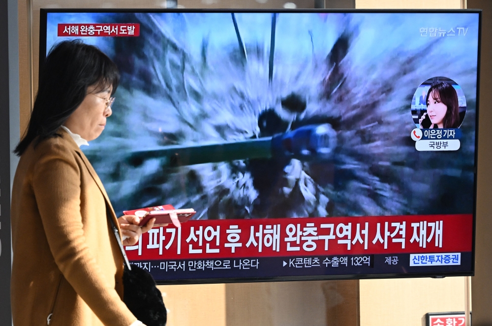 A woman walks past a television screen showing a news broadcast with file footage of North Korea's artillery firing, at a railway station in Seoul January 5, 2024. — AFP pic 