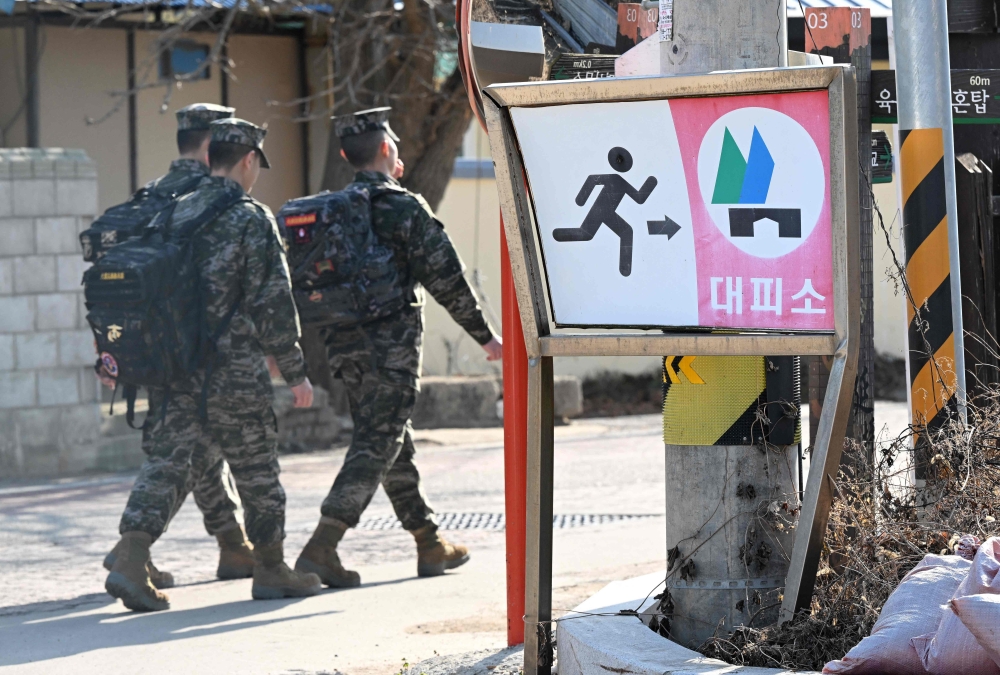 South Korean marines walk past a shelter sign in a village of Yeonpyeong island. — AFP pic