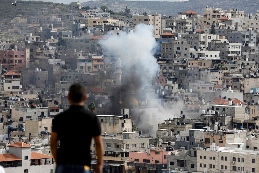 A man looks on as smoke billows above buildings in the Nur Shams camp for Palestinian refugees near the occupied West Bank city of Tulkarm, during an ongoing Israeli raid January 4, 2024. — AFP pic