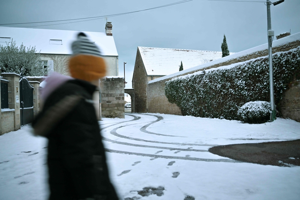A woman walks along a residential street following overnight snow fall, in Courseulles-sur-Mer January 9, 2024. — AFP pic 