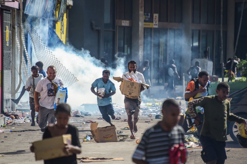 People run with merchandise as crowds leave shops with looted goods amid a state of unrest in Port Moresby on January 10, 2024. — AFP pic