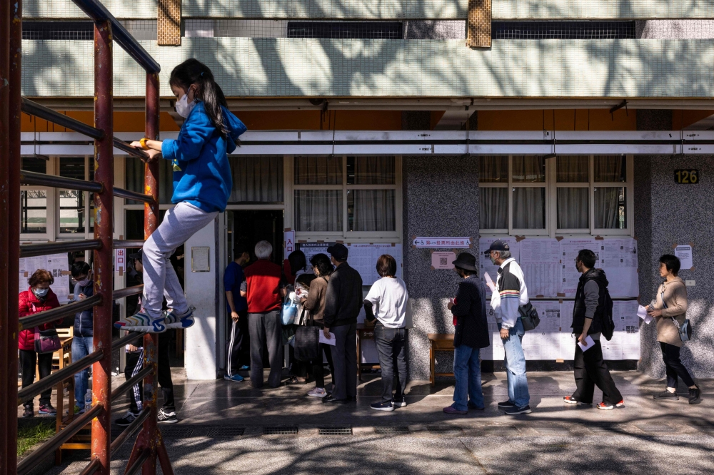 A child plays as people wait in line to cast their ballots and vote in the presidential election at a polling station at an elementary school in New Taipei City January 13, 2024. — AFP pic