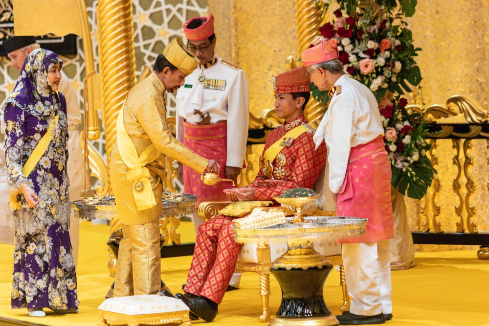 This photograph taken on January 10, 2024 shows Brunei's Sultan Hassanal Bolkiah pouring scented oil on the hands of Prince Abdul Mateen during the royal powdering ceremony at Istana Nurul Iman, ahead of his wedding to Anisha Rosnah, in Bandar Seri Begawan, as Queen Raja Isteri Pengiran Anak Hajah Saleha looks on. — AFP pic