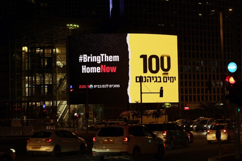 Cars drive past a giant board reading the slogan ‘bring them home now’ and the number 100 in central Tel Aviv, on January 13, 2024, after almost 100 days of war between Israel and the militant Hamas group in Gaza. — AFP pic