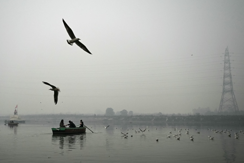 People ride a boat across river Yamuna on a cold winter morning in New Delhi on January 13, 2024. — AFP pic