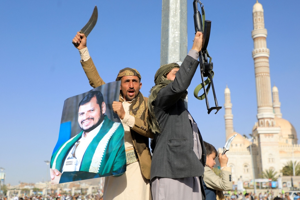 Protesters, one holding a portrait of Houthi leader Abdul Malik al-Houthi, brandish their weapons during a protest following US and British forces strikes. — AFP pic