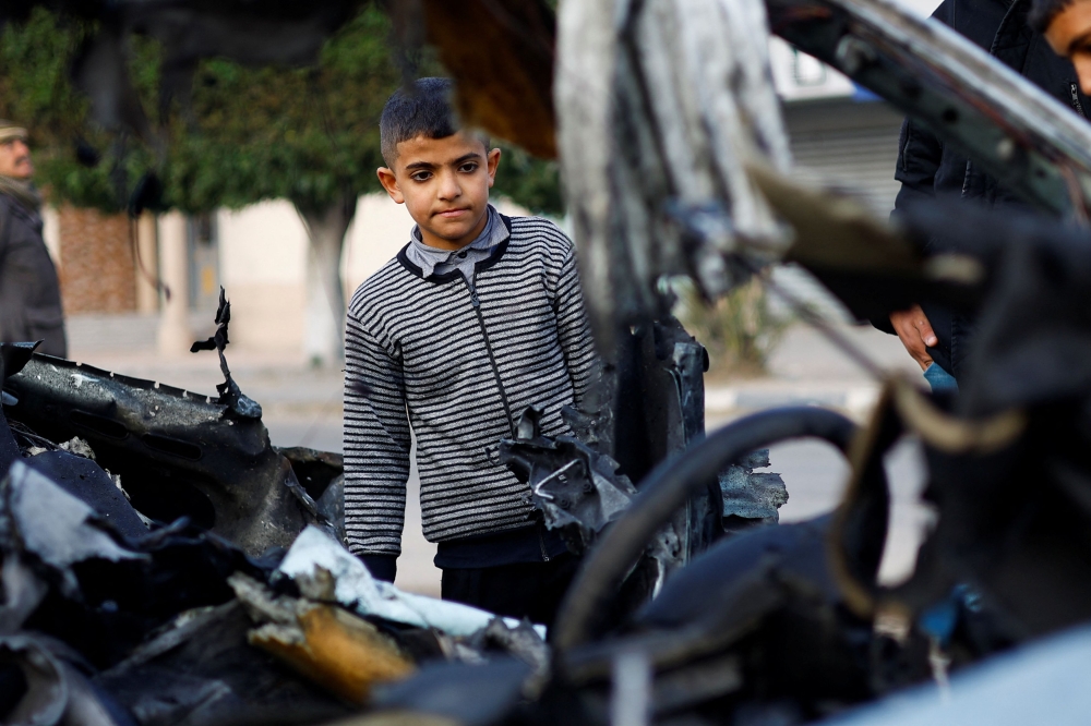 A Palestinian boy inspects the remains of a car in the aftermath of an Israeli strike, amid the ongoing conflict between Israel and the Palestinian Islamist group Hamas, in Rafah in the southern Gaza Strip, January 21, 2024. — Reuters pic