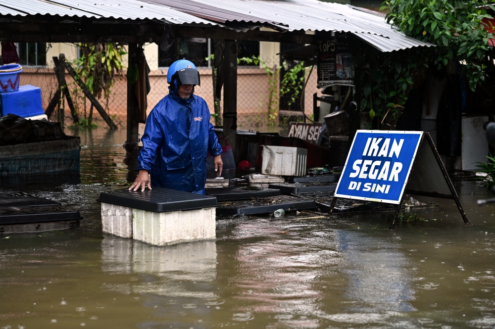 A trader moves a box of fish after his stall was inundated with water after heavy rain in Jalan Kamaruddin, Kuala Terengganu, January 23, 2024. — Bernama pic 