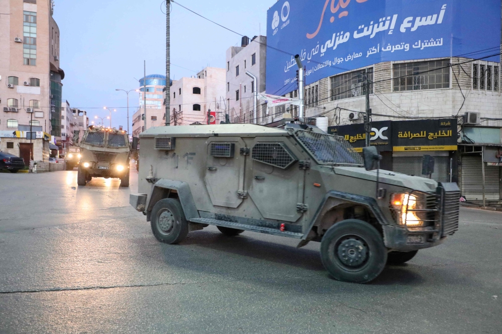 Israeli forces drive armoured vehicles down a road during a raid in Hebron city in the occupied West Bank. — AFP pic