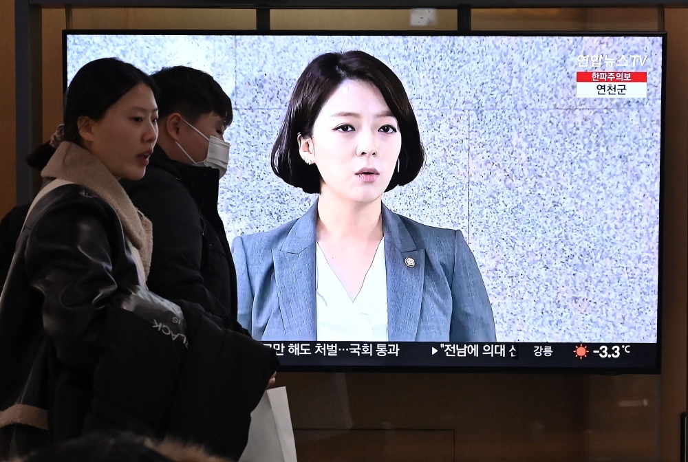 People walk past a television screen showing a news broadcast with a file footage of lawmaker Bae Hyun-jin. — AFP pic