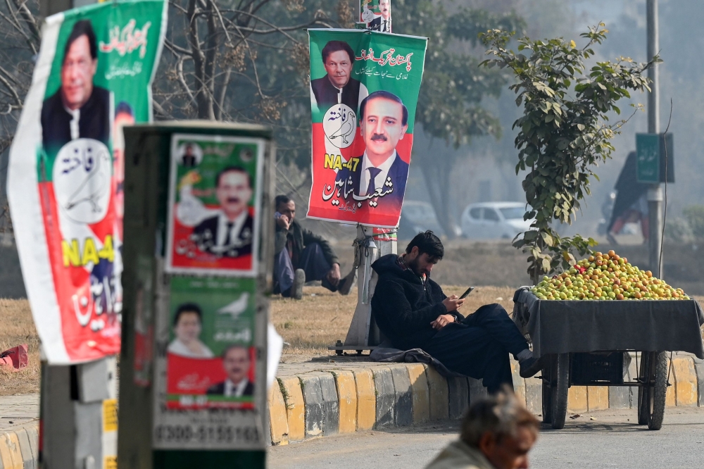 A vendor sits next to a poster of a Pakistan Tehreek-e-Insaf (PTI) party  indpendent candidate Shoaib Shaheen along a street in Islamabad on January 24, 2024, ahead of the country's upcoming general election. — AFP pic
