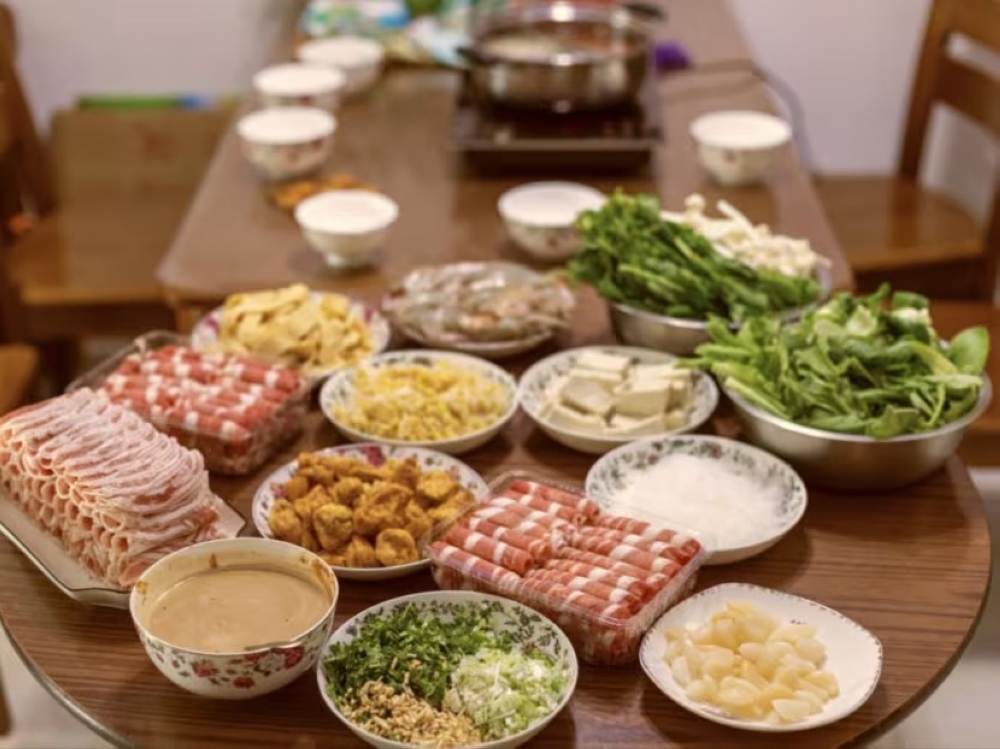 Fried and raw food items, along with peanut sauce for dipping, are set at a dining table, ready to be cooked in a hot pot of soup or broth for a communal meal. — iStock pic via TODAY
