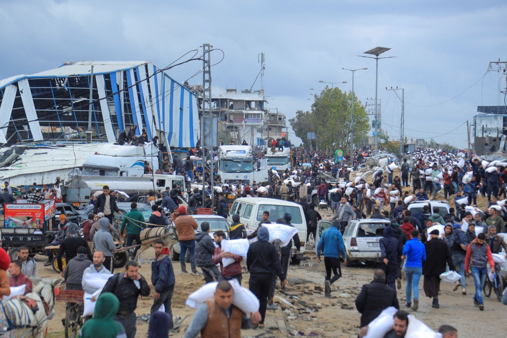 Palestinians carry bags of flour they grabbed from an aid truck near an Israeli checkpoint, as Gaza residents face crisis levels of hunger. — Reuters pic