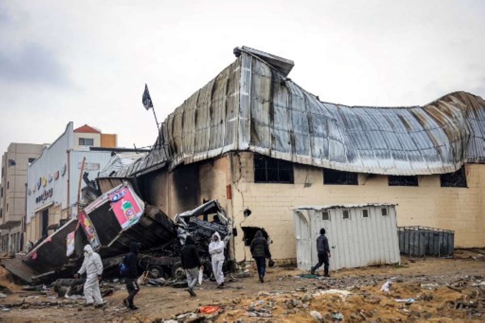 Palestinians, some wearing hazmat suits left over from the Covid pandemic, walk past a fire-damaged UNRWA (United Nations Relief and Works Agency for Palestine Refugees) warehouse in Khan Yunis. — AFP pic