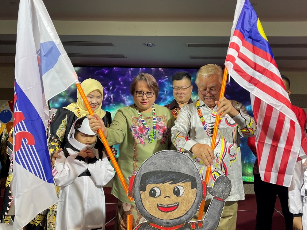 Sikie (right) and Roselind affix the Jalur Gemilang and Kemas flags to the event’s icon to mark the launching of the event. — Borneo Post pic