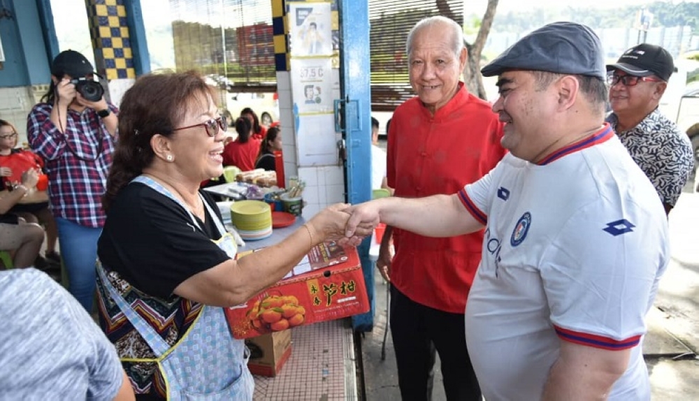 Shahelmey presenting a box of oranges to a restaurant operator in Tanjung Aru during the walkabout. — Borneo Post Online pic