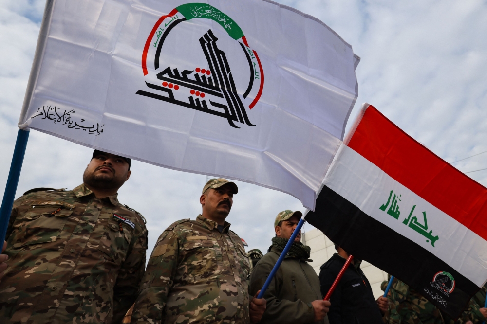 Members of Iraq's Hashed al-Shaabi (Popular Mobilisation), carry their flag as well as that of Iraq, ahead of the funeral of people killed the previous day in US strikes in western Iraq, in Baghdad on January 4, 2024. — AFP pic