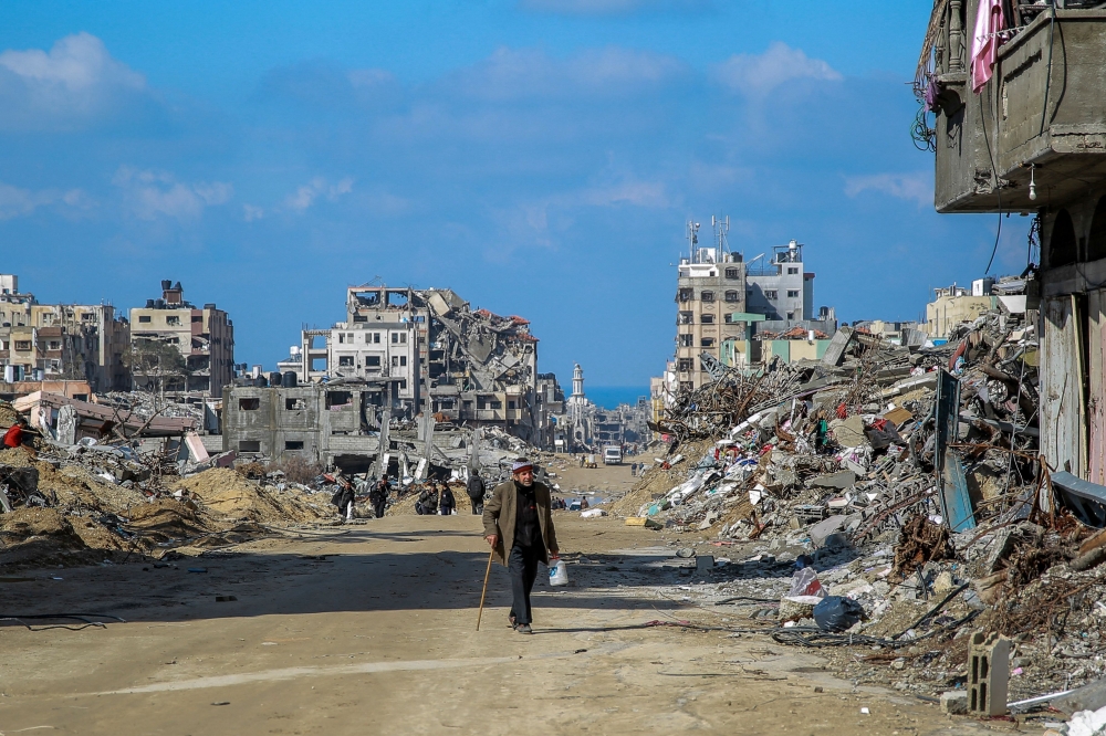 People walk along Al-Oyoun Street amid the rubble of buildings destroyed as Israel continues to bomb Gaza. 