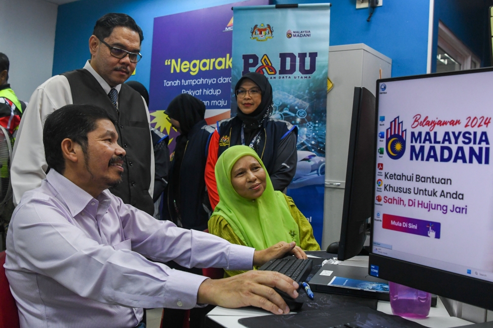 Chief Statistician Datuk Seri Mohd Uzir Mahidin (seated left) assists a resident with the Padu registration process in the Digital Economy Centre (PEDi) in Mahligai, Bachok February 7, 2024. — Bernama pic