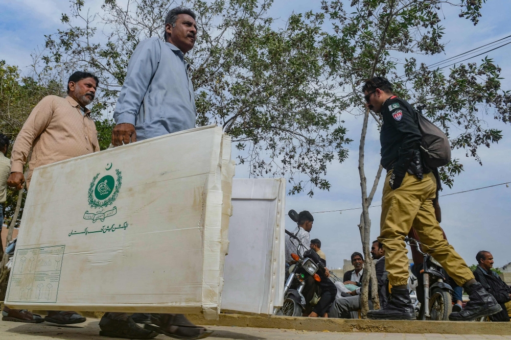 Election presiding officers walk past a policeman as they leave after collecting voting materials at a distribution center in Karachi on February 7, 2024, a day prior Pakistan's  national elections. — AFP pic