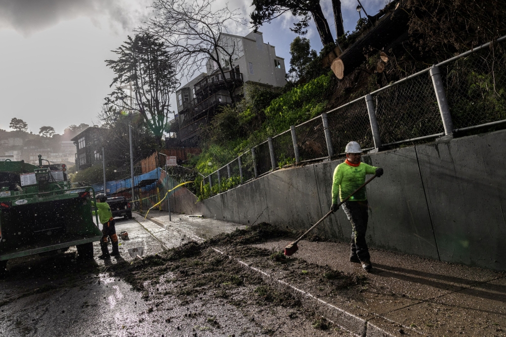 Workers clear an area of a fallen tree as a Pacific storm known as an 
